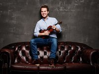 Lächelnder Mann mit Geige sitzt auf einer klassischen Chesterfield Couch