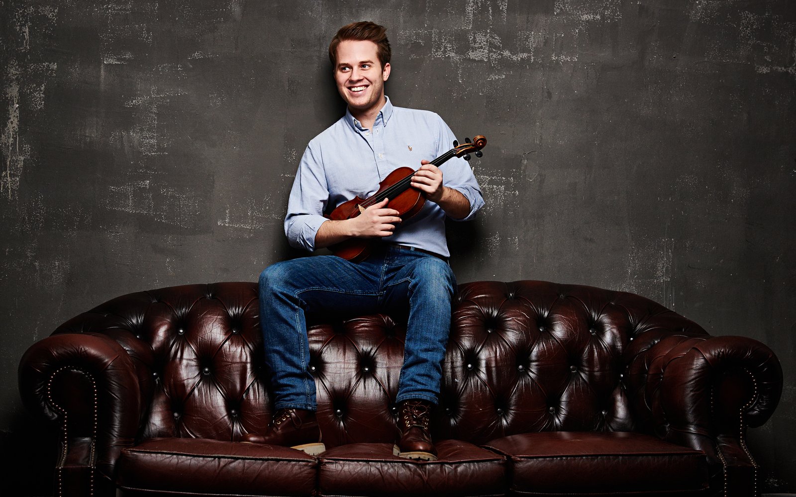 Lächelnder Mann mit Geige sitzt auf einer klassischen Chesterfield Couch